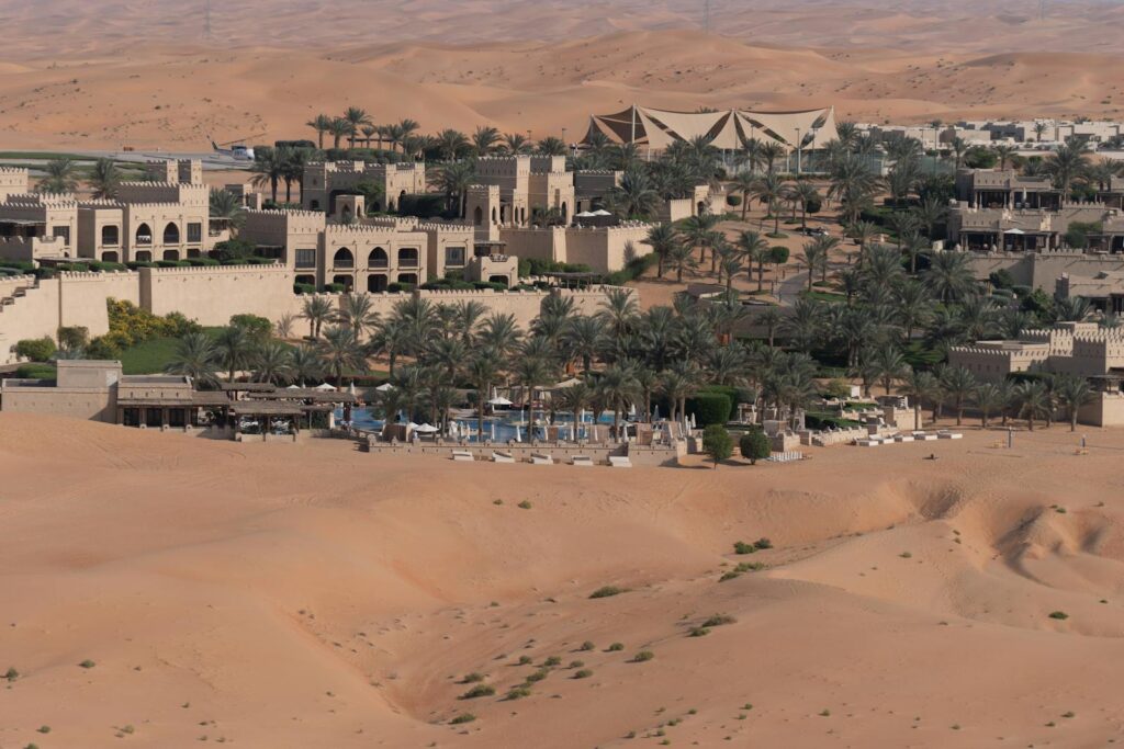 Aerial view of a luxurious desert oasis resort surrounded by vast sandy dunes and palm trees.